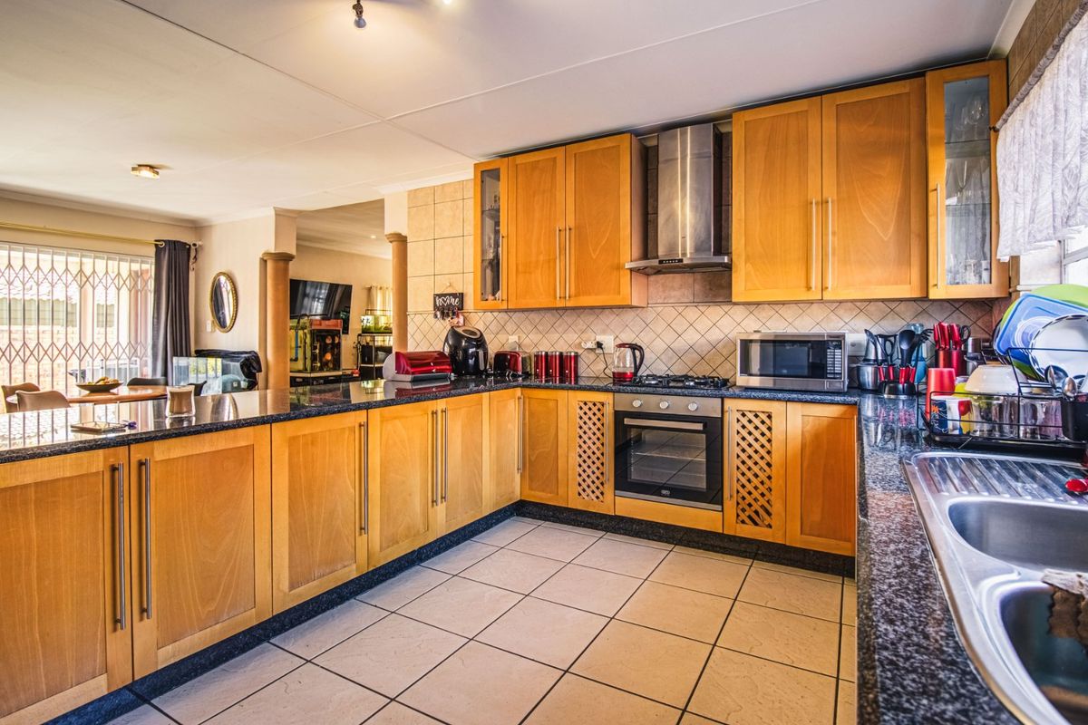 A functional kitchen featuring wooden cabinetry, granite countertops, a built-in oven with gas hob, and a stainless steel extractor fan.