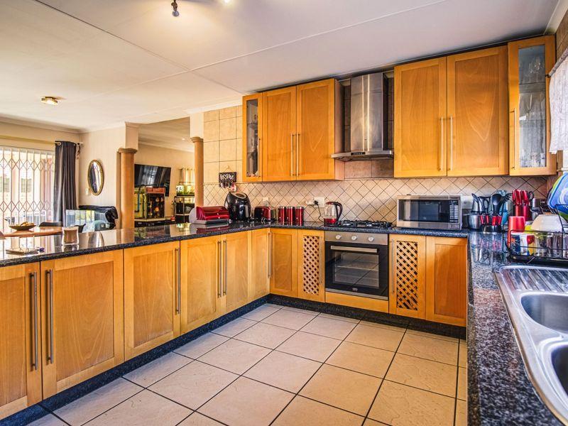 A functional kitchen featuring wooden cabinetry, granite countertops, a built-in oven with gas hob, and a stainless steel extractor fan.