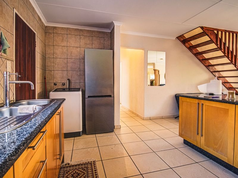 A functional kitchen featuring wooden cabinetry, granite countertops, tiled backsplash, and an integrated staircase leading to the upper level.