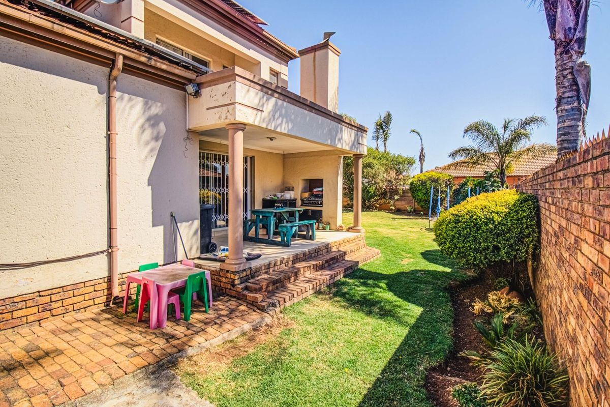 Rear view of the house featuring a covered patio with a built-in braai, brick paving, and a spacious garden with a brick boundary wall.