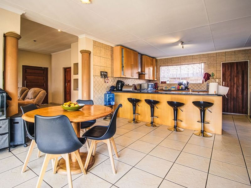 Open plan kitchen and dining area featuring tiled flooring, wooden cabinetry, granite countertops, and a breakfast bar with integrated seating.