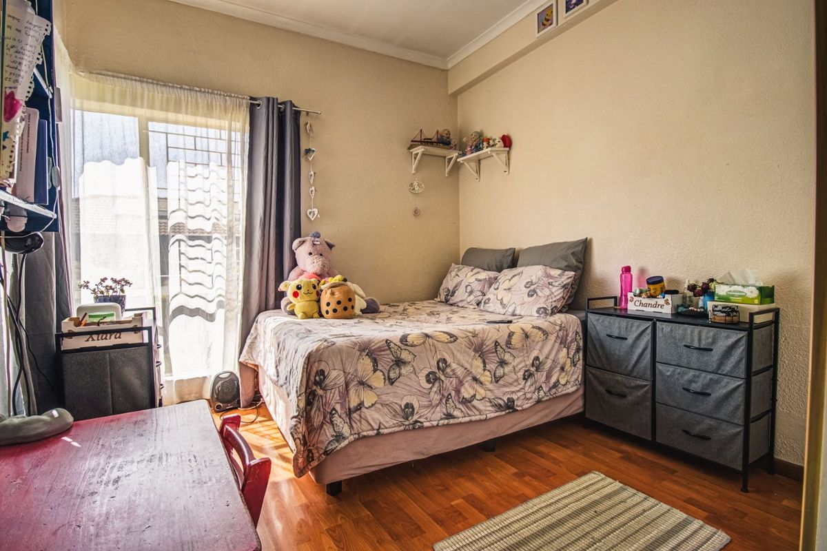 A functional bedroom featuring laminate flooring, a sliding window with security gate, and neutral wall finishes.