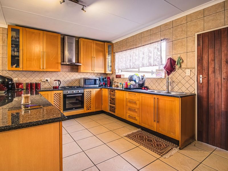 A functional kitchen featuring wooden cabinetry, granite countertops, a built-in oven with gas hob, and a tiled backsplash.