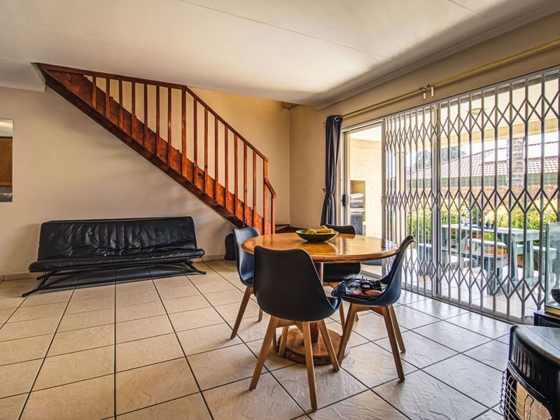 Open plan living and dining area featuring tiled flooring, a wooden staircase, and sliding glass doors leading to an outdoor patio space.