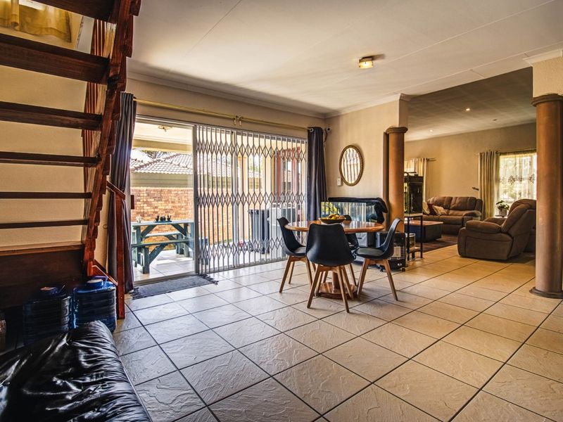 Open plan living and dining area featuring tiled floors, a wooden staircase, and sliding doors leading to an outdoor patio space.