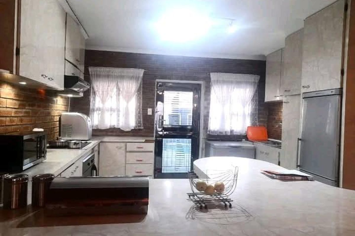 A functional kitchen featuring built-in cabinetry, stone-look countertops, an integrated oven, and a distinctive exposed brick wall with natural light.