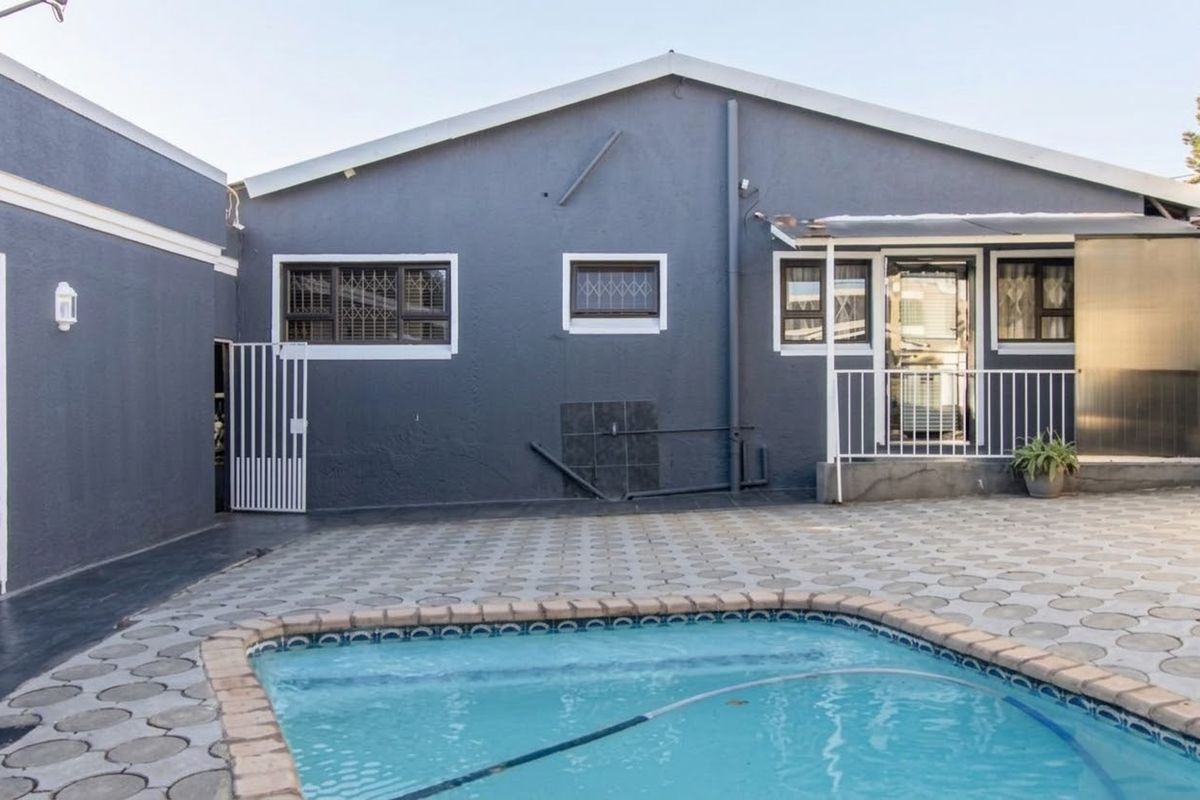 Rear exterior view featuring a swimming pool, paved patio area, and a grey rendered facade with security bars on windows.