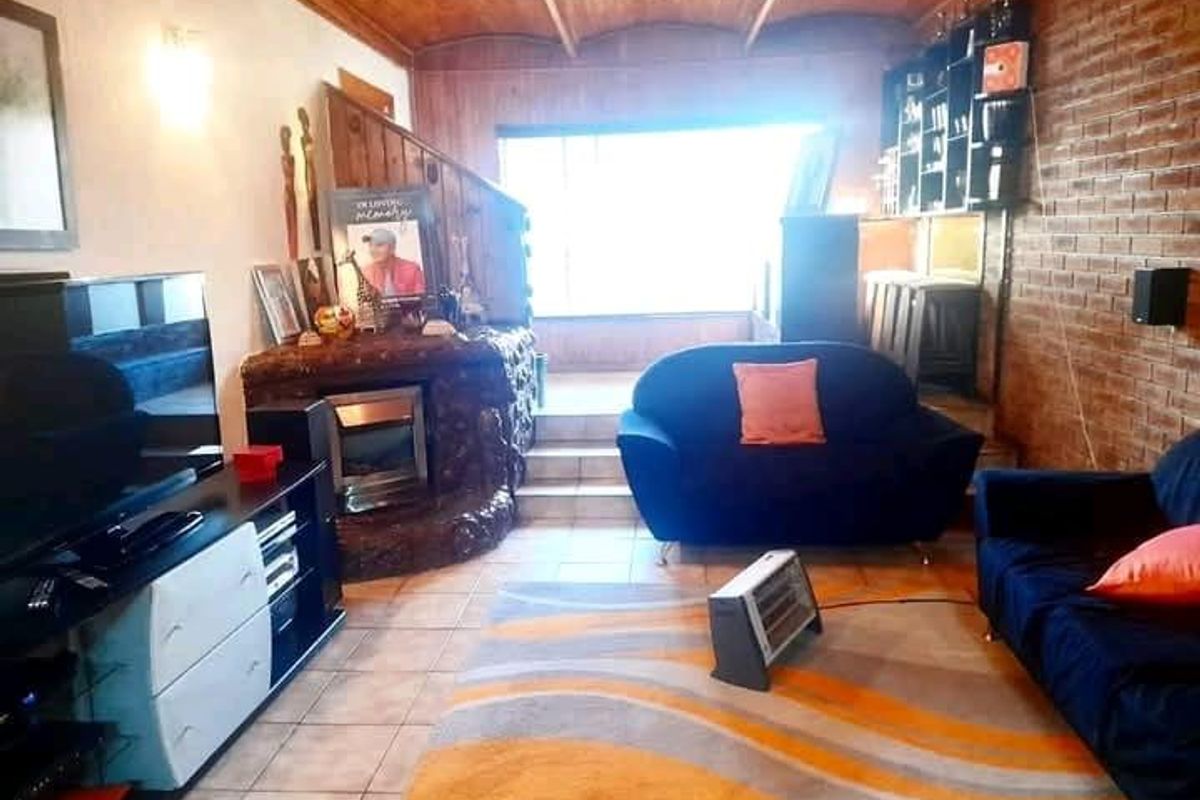 Living room featuring exposed brick walls, a timber panelled ceiling, tiled flooring, and a built-in fireplace, offering a rustic aesthetic with potential for modernization.