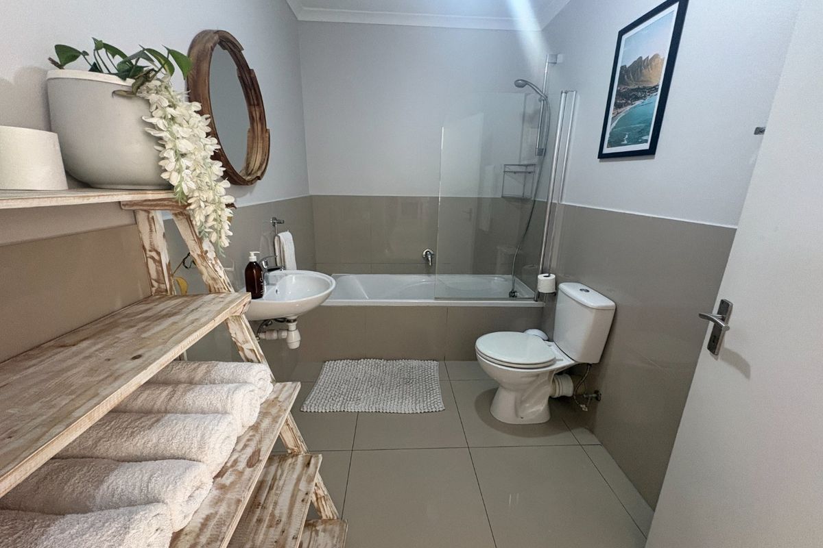A clean and functional bathroom featuring a bathtub with a glass shower screen, a pedestal basin, and a standard toilet with neutral wall tiling.