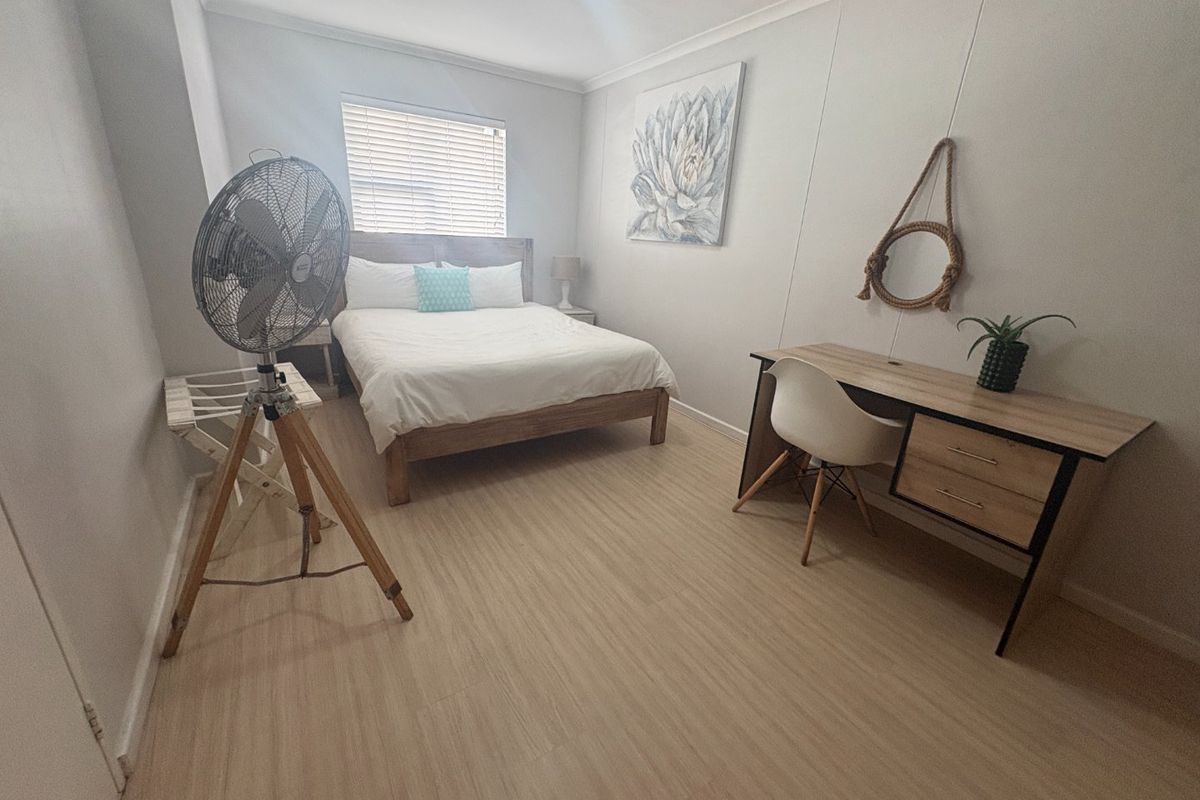 A well-maintained bedroom featuring light-toned laminate flooring, neutral walls, and venetian blinds, offering a clean and functional living space.