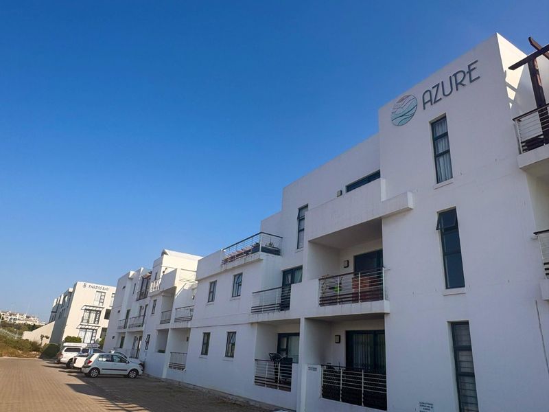 Exterior view of the Azure apartment complex, featuring modern white facade, private balconies with metal railings, and clear blue sky.