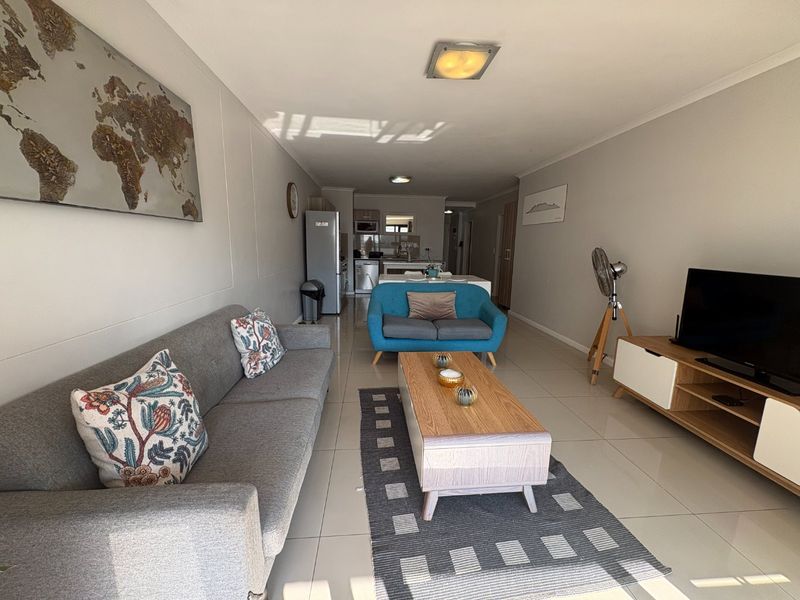 An open-plan living and kitchen area featuring neutral tiled flooring, modern cabinetry, and a functional layout suitable for contemporary apartment living.
