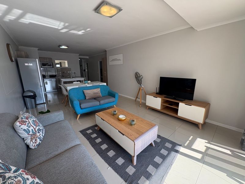 An open-plan living and kitchen area featuring neutral wall tones, tiled flooring, and functional built-in cabinetry, offering a bright and cohesive living space.