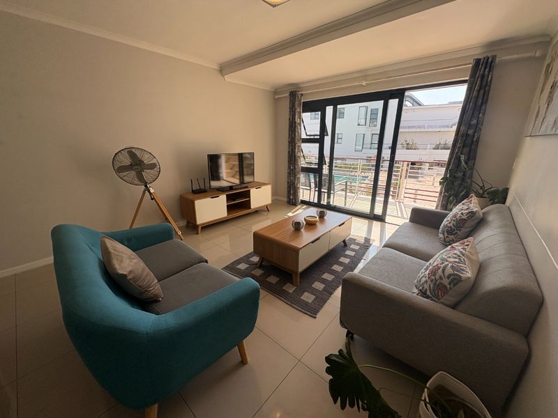 A bright living room featuring tiled flooring and large sliding glass doors that provide access to an outdoor balcony area.