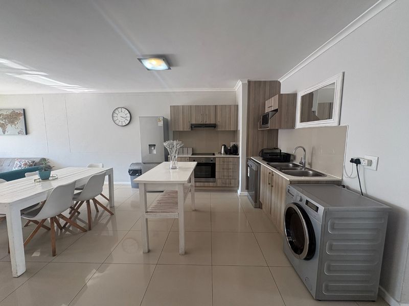 Open-plan living and kitchen area featuring modern wood-finish cabinetry, integrated appliances, and neutral tiled flooring throughout the space.