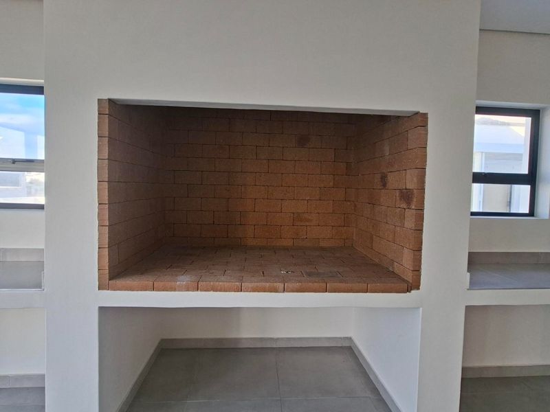 A clean, covered patio area featuring a built-in brick braai, tiled flooring, and integrated concrete counter space, ready for outdoor entertaining.