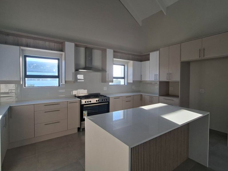 Modern kitchen featuring sleek cabinetry, stone countertops, a central island, and high-quality stainless steel appliances in a bright, open-plan space.