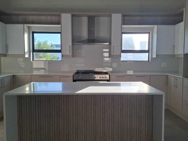 Modern kitchen featuring a central island, quartz countertops, stainless steel gas stove, extractor fan, and ample built-in cabinetry.