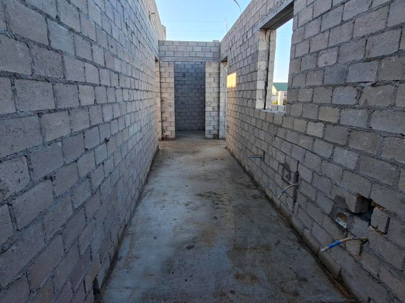 An unfinished hallway interior showing exposed concrete block walls, concrete flooring, and rough-in plumbing conduits in a property under construction.