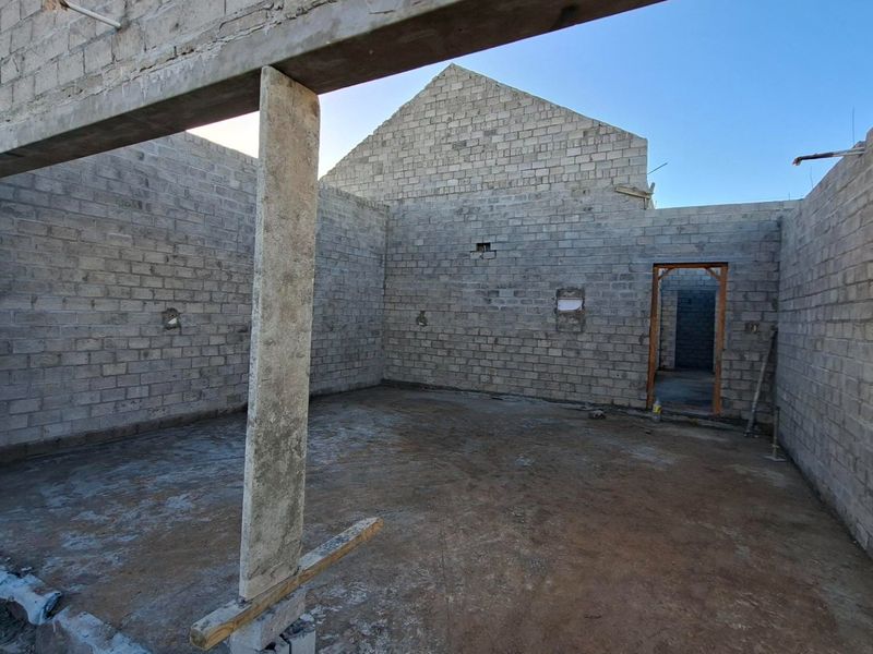 An unfinished open-plan interior space featuring exposed concrete block walls, structural beams, and columns, currently in the early stages of construction.