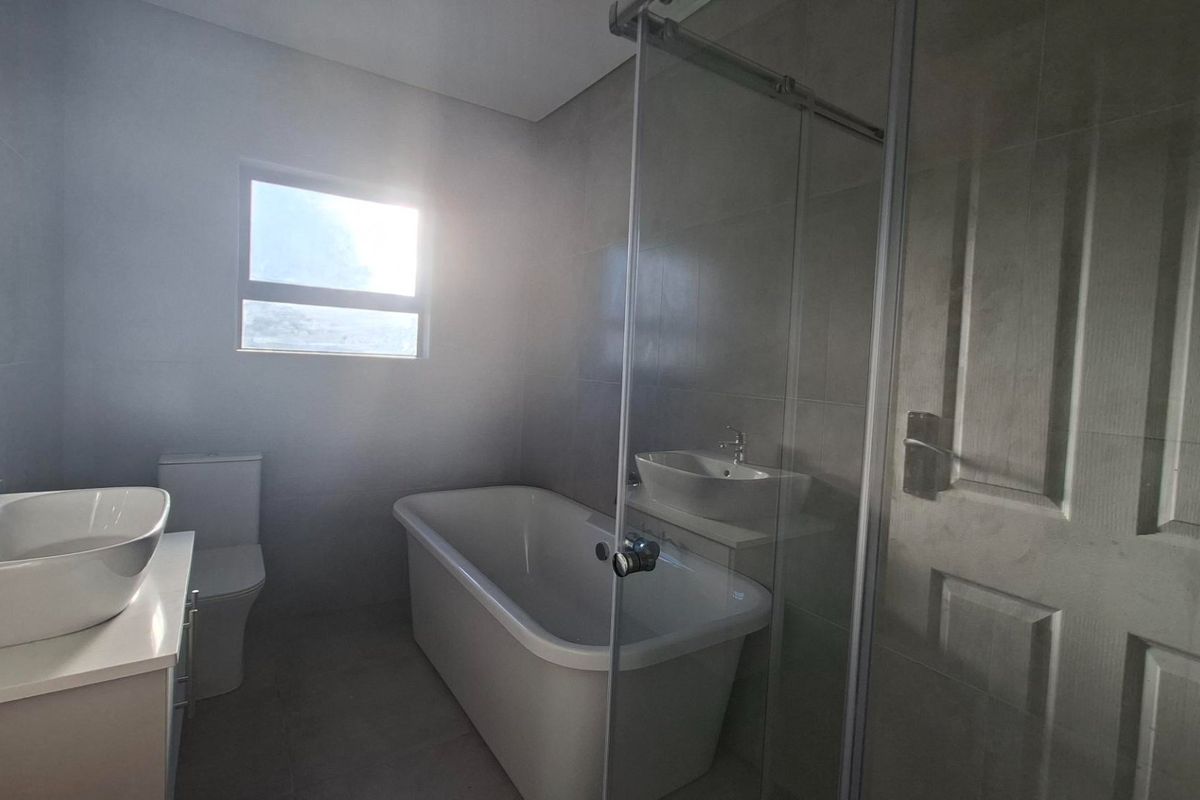 Modern bathroom featuring a freestanding bathtub, glass-enclosed shower, vanity basin, and neutral floor-to-ceiling tiling.