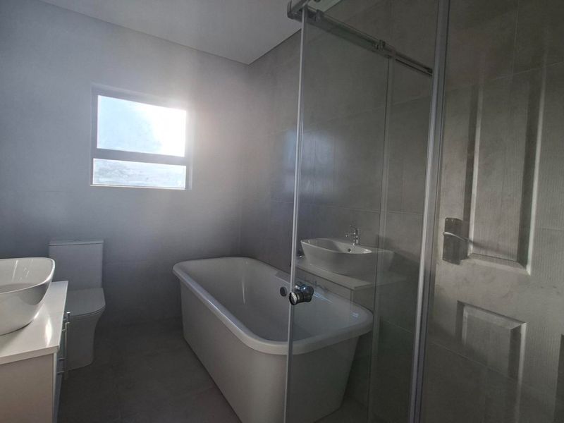 Modern bathroom featuring a freestanding bathtub, glass-enclosed shower, vanity basin, and neutral floor-to-ceiling tiling.