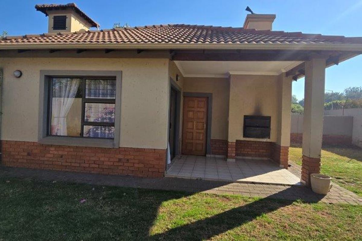 Rear view of the townhouse featuring a covered patio with a built-in braai, tiled roof, and a private garden area.
