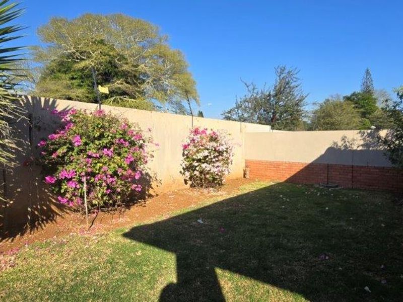 A private rear garden featuring a lawn, paved walkway, and perimeter boundary wall with established flowering shrubs.
