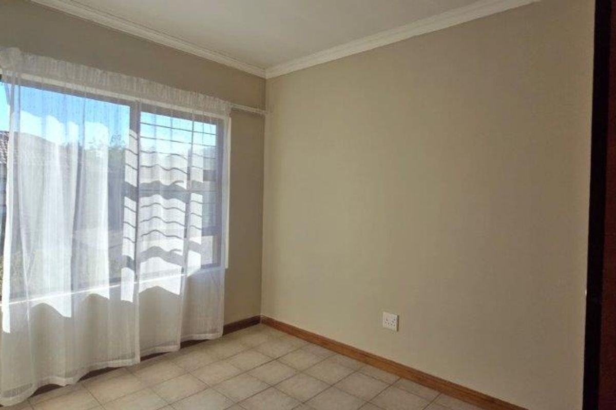 A clean, empty bedroom featuring neutral wall tones, tiled flooring, and a built-in cupboard, offering a versatile space ready for personalization.
