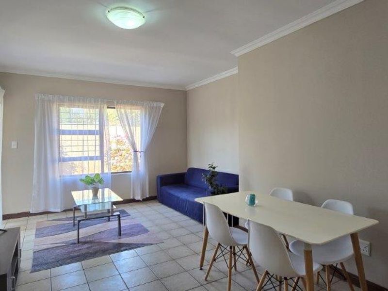 Open-plan living and dining area featuring tiled flooring, coved ceilings, and a window with security bars, providing a functional and well-lit space.