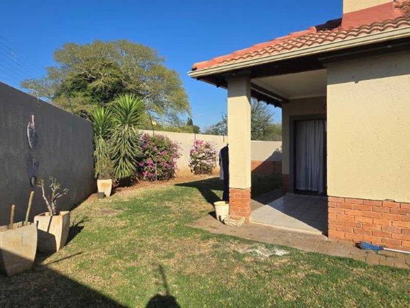 Rear view of the townhouse featuring a covered patio, brick and plaster facade, tiled roof, and a private garden enclosed by a perimeter wall.