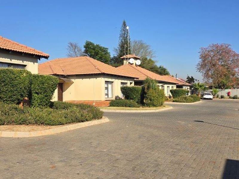 A view of the townhouse complex exterior featuring paved driveways, well-maintained garden beds, and traditional terracotta tiled roofs.