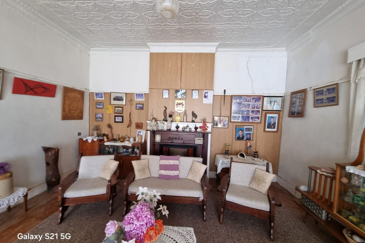 A living room featuring a traditional pressed metal ceiling, timber wall paneling, and a fireplace mantel, showing signs of wear and structural cracking.