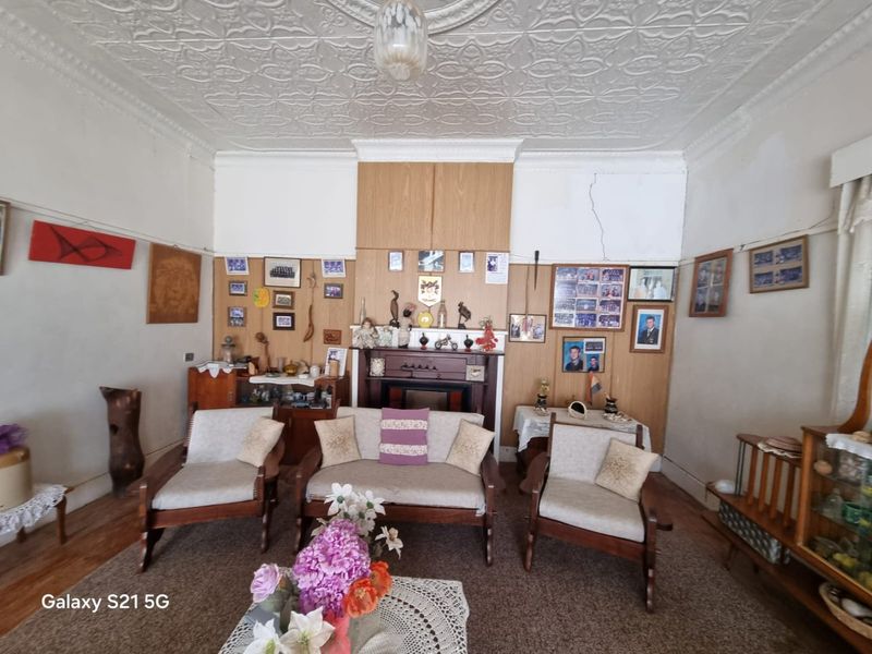 A living room featuring a traditional pressed metal ceiling, timber wall paneling, and a fireplace mantel, showing signs of wear and structural cracking.
