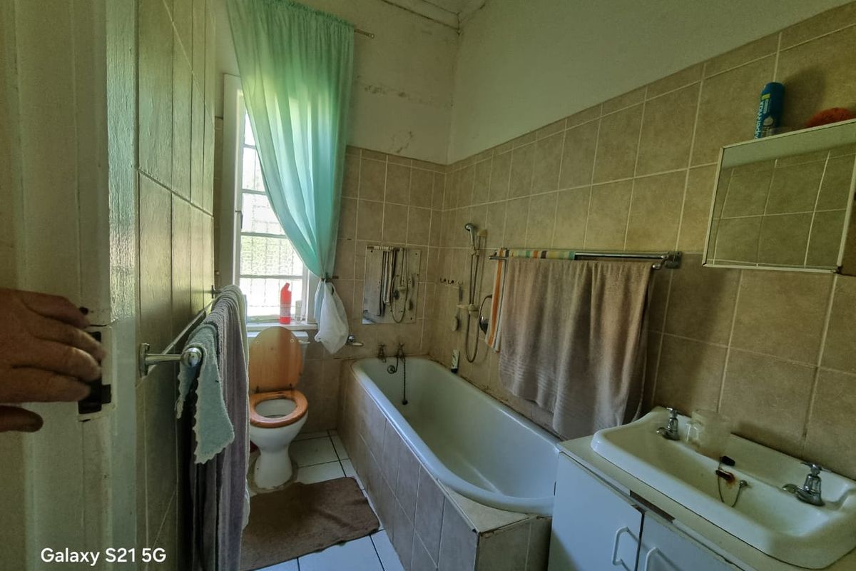 A dated bathroom featuring a bathtub, toilet, and vanity basin with tiled walls and flooring, requiring cosmetic updates and maintenance.
