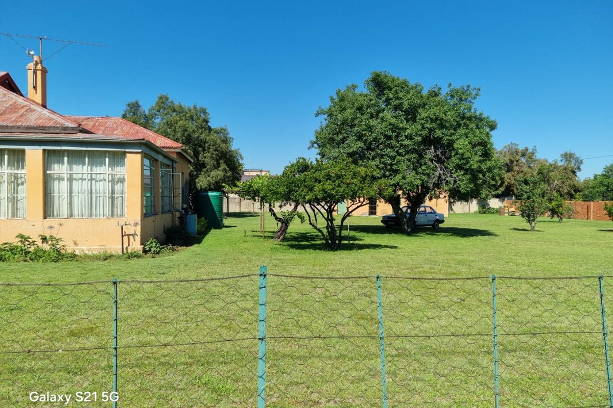 A view of the rear exterior of the house featuring a corrugated metal roof, chimney, and a large garden area with a wire fence.
