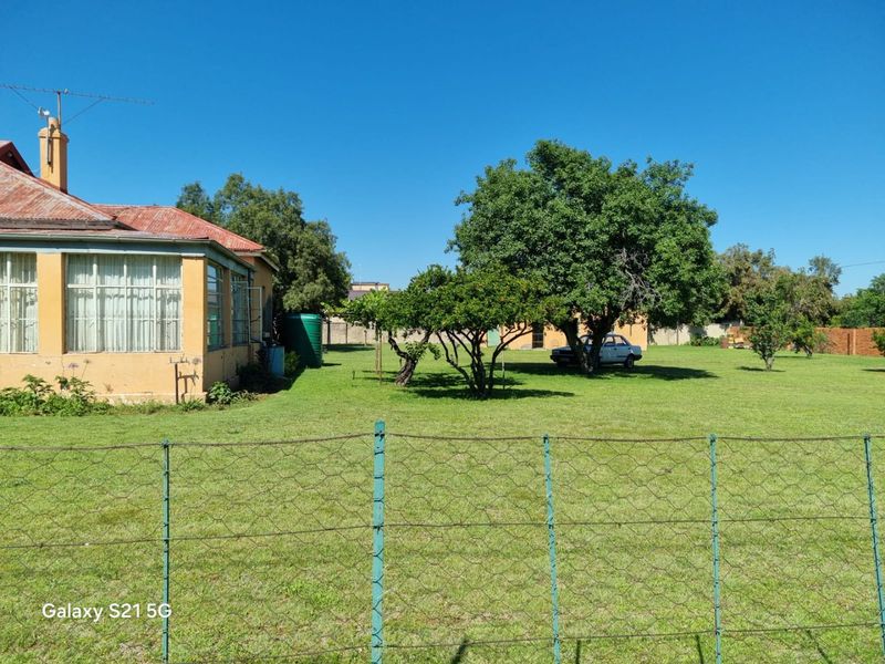 A view of the rear exterior of the house featuring a corrugated metal roof, chimney, and a large garden area with a wire fence.