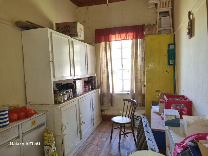 A dated scullery or utility area featuring original built-in cabinetry, timber flooring, and a window, requiring significant renovation and cosmetic updates.