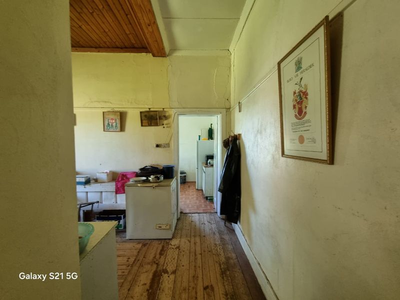 A hallway area featuring timber flooring and a wood-paneled ceiling, showing signs of wear and requiring maintenance to the wall finishes.