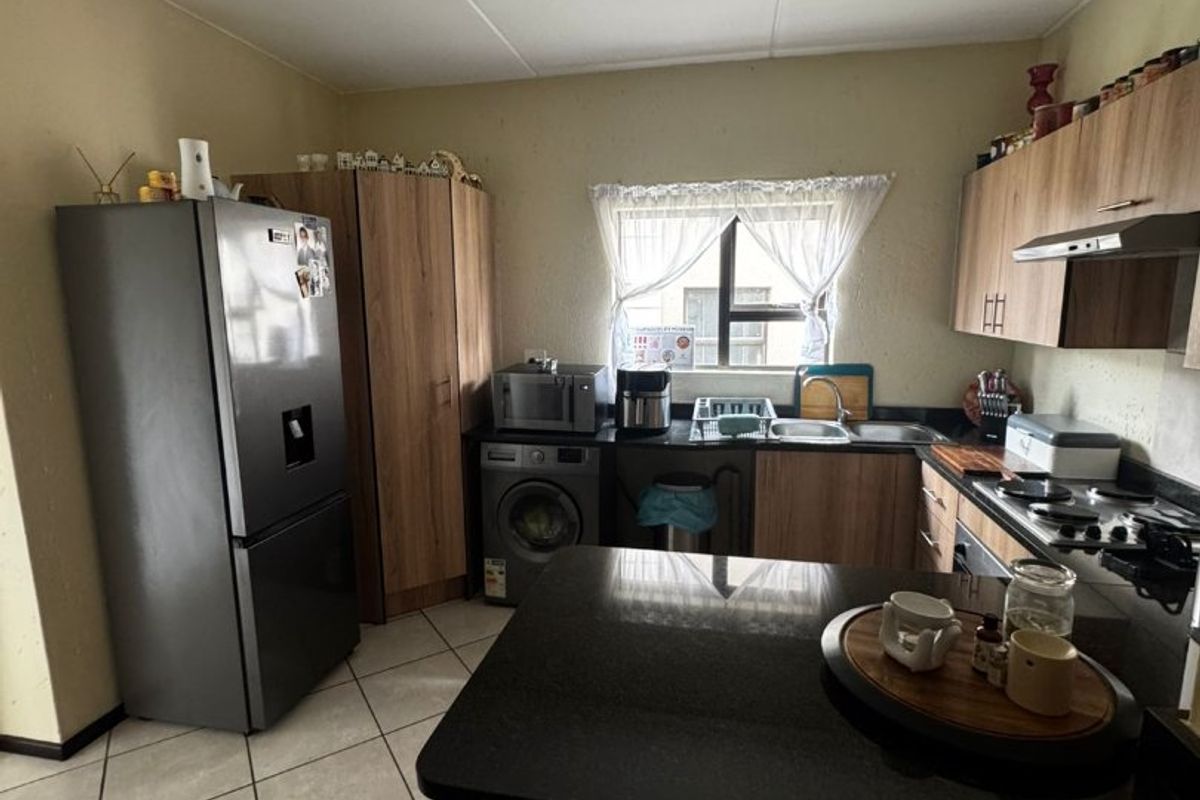 Functional kitchen featuring wood-finish cabinetry, granite countertops, a gas hob, extractor fan, and tiled flooring with space for integrated appliances.