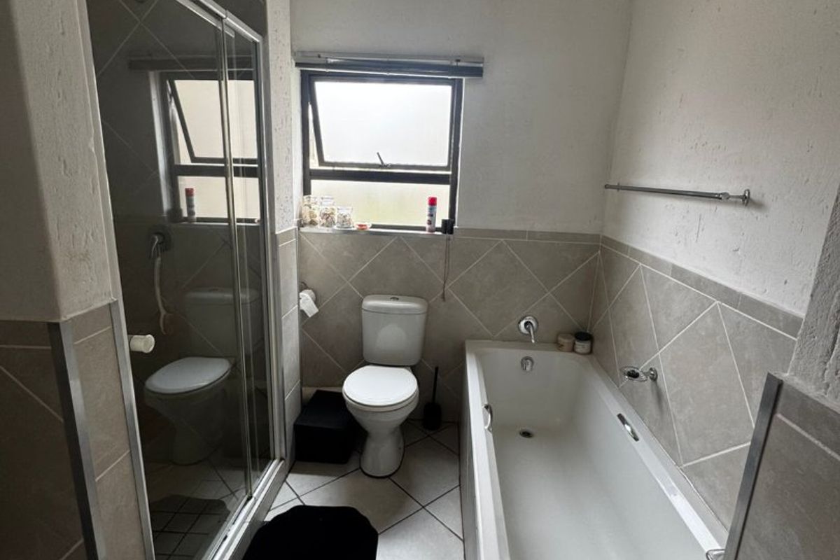 A functional bathroom featuring a bathtub, separate shower enclosure, and toilet with neutral tiled finishes and natural light from a top-hung window.