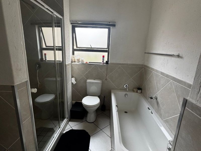 A functional bathroom featuring a bathtub, separate shower enclosure, and toilet with neutral tiled finishes and natural light from a top-hung window.