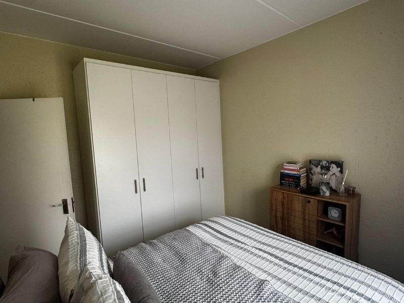 A functional bedroom featuring a white built-in wardrobe and neutral wall finishes, providing a practical and comfortable sleeping space.