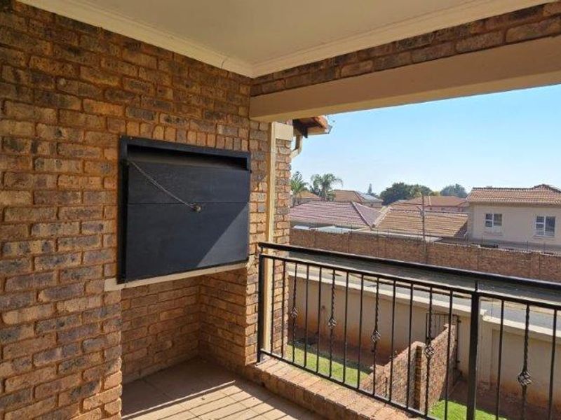 Covered balcony featuring a built-in braai, exposed brick wall, and metal balustrade with views over the surrounding residential area.
