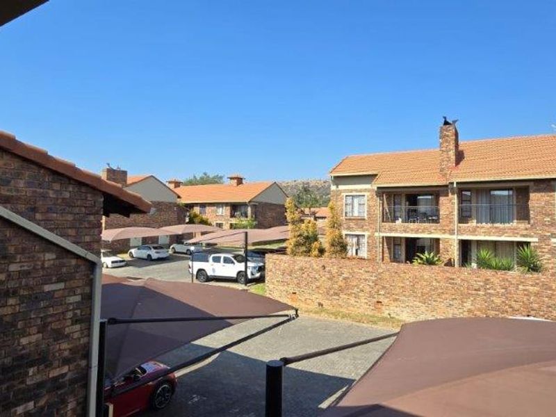 View of the apartment complex exterior featuring face brick buildings, tiled roofs, and designated shade cloth parking bays within the estate.