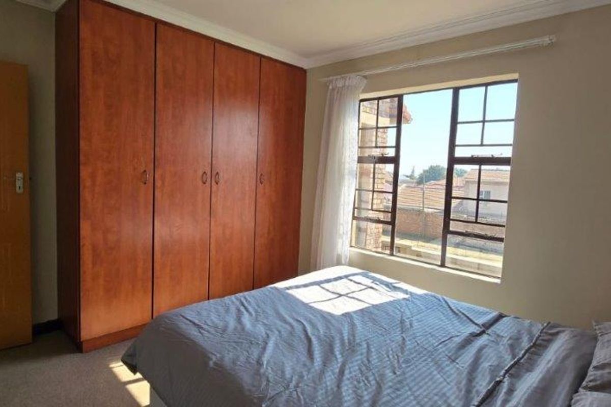 A bedroom featuring built-in wooden cupboards, carpeted flooring, and a steel-framed window allowing natural light.