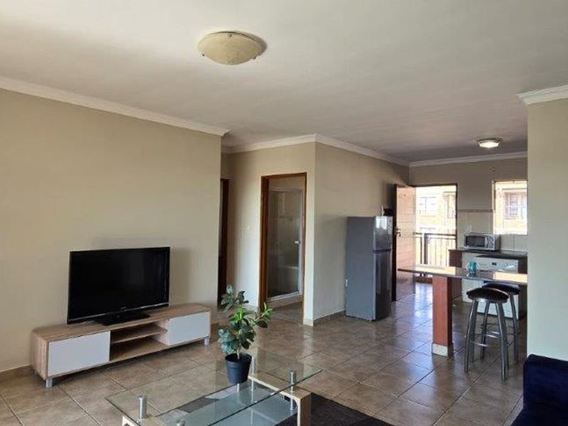 Open-plan living area featuring tiled flooring, a functional kitchen with a breakfast counter, and direct access to an outdoor balcony.