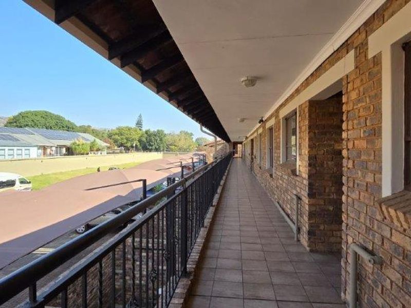 An exterior walkway or balcony featuring exposed brick walls, tiled flooring, and a wrought iron balustrade overlooking the parking area.