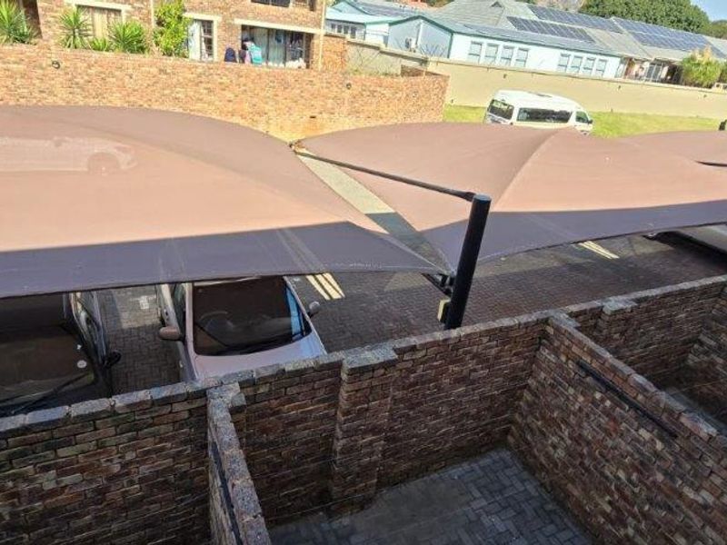 Outdoor parking area featuring multiple shade cloth carports and brick partition walls on a paved surface.