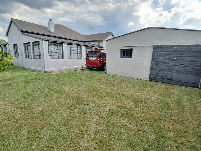 Rear view of the property featuring a lawn, detached garage, and main house structure with a pitched roof and chimney.